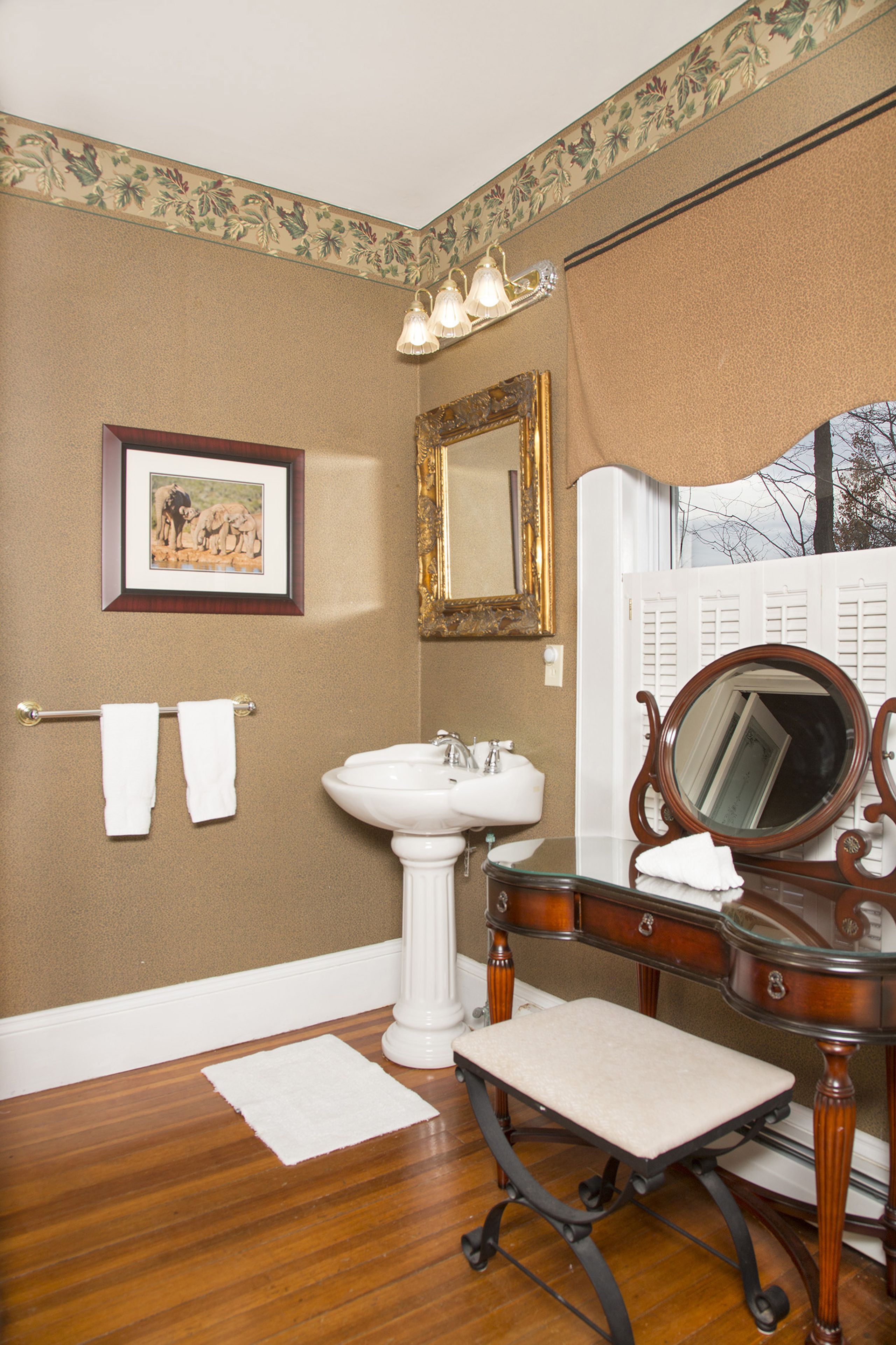 A bathroom with a wooden floor, a white sink, a mirror, and a framed picture on the wall.
