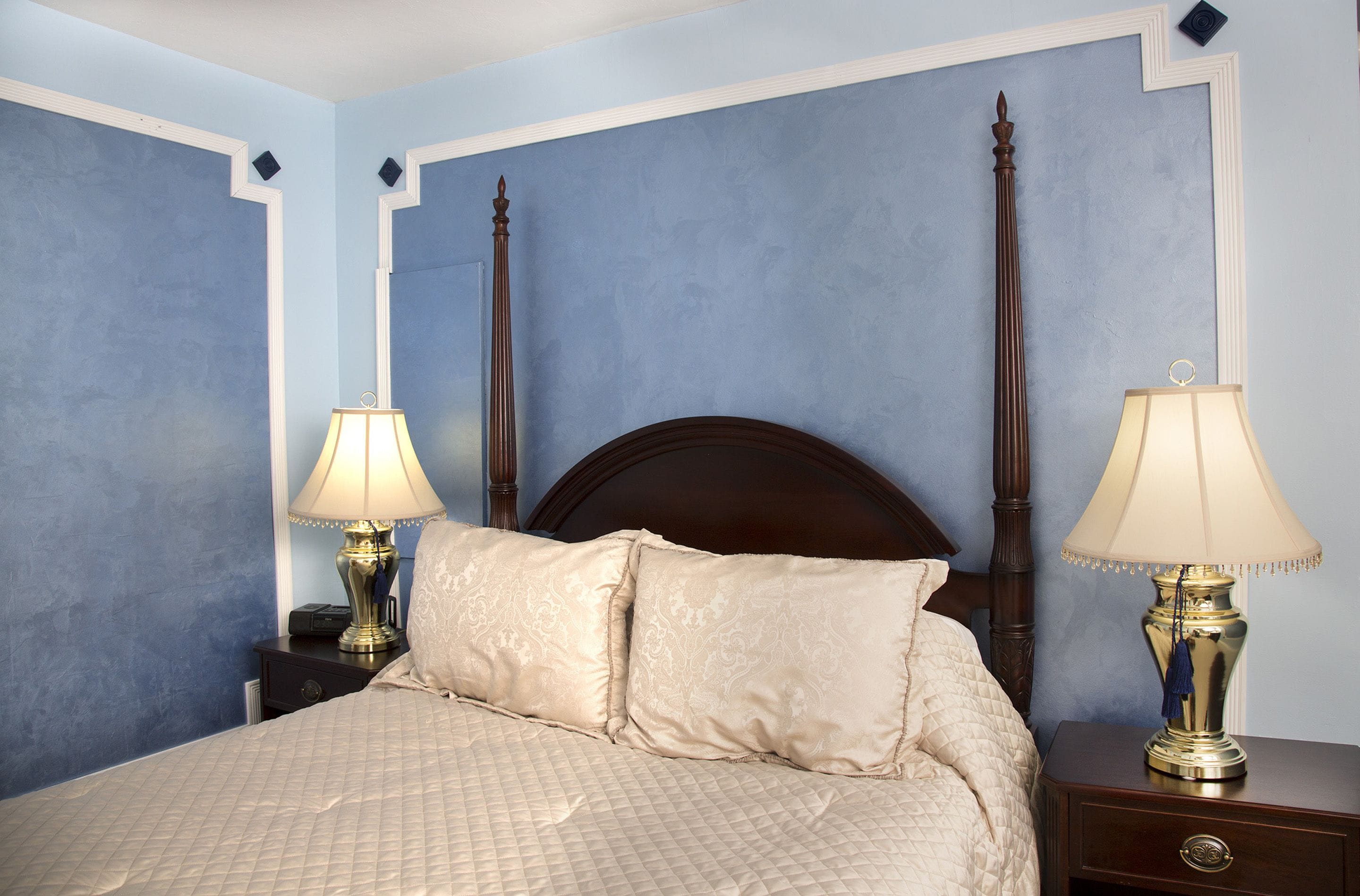 A neatly made bed with a quilted bedspread and two decorative pillows, flanked by two bedside tables with lamps.