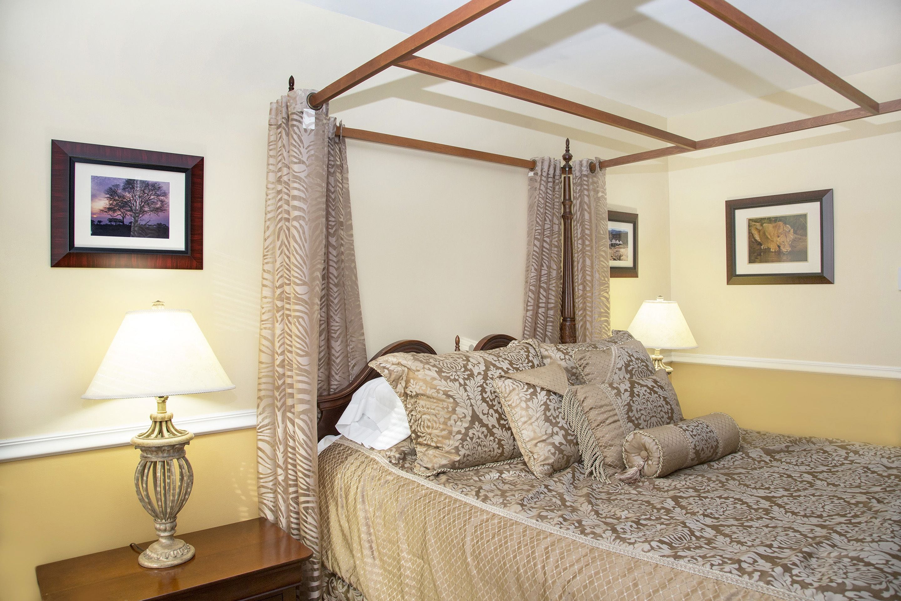 A four-poster bed with a canopy, a bedside table with a lamp, and two framed pictures on the wall.