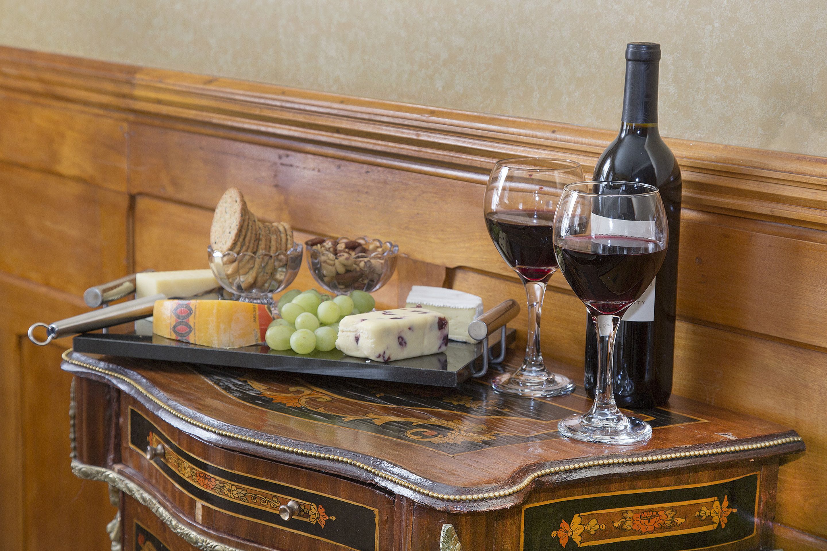 A wooden table with a cheese platter, grapes, and wine glasses.