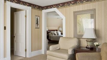 A hotel room with a beige armchair, a wooden nightstand with a lamp, and a framed picture on the wall.