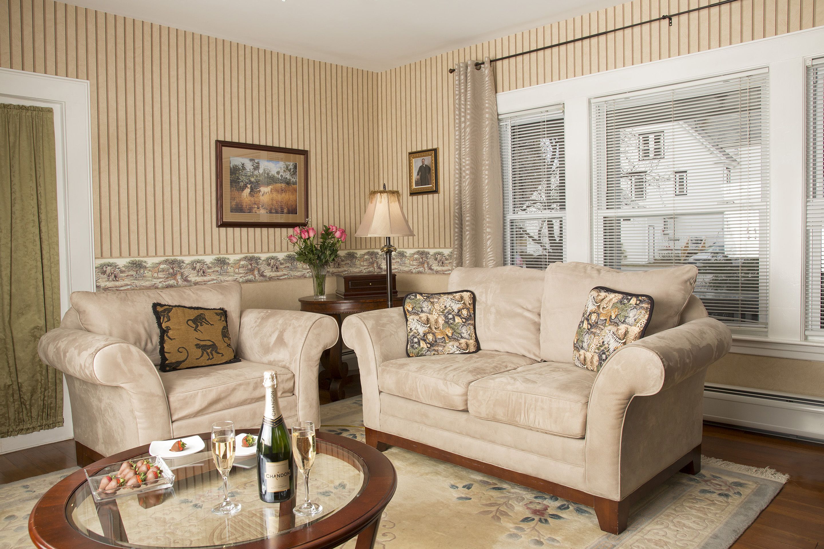 A living room with two beige sofas, a coffee table with a bottle and glasses, and a floral rug.