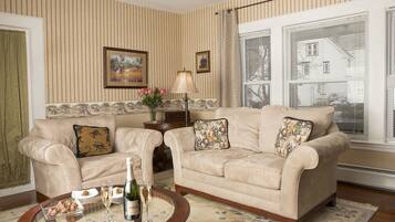 A living room with two beige sofas, a coffee table with a bottle and glasses, and a floral rug.