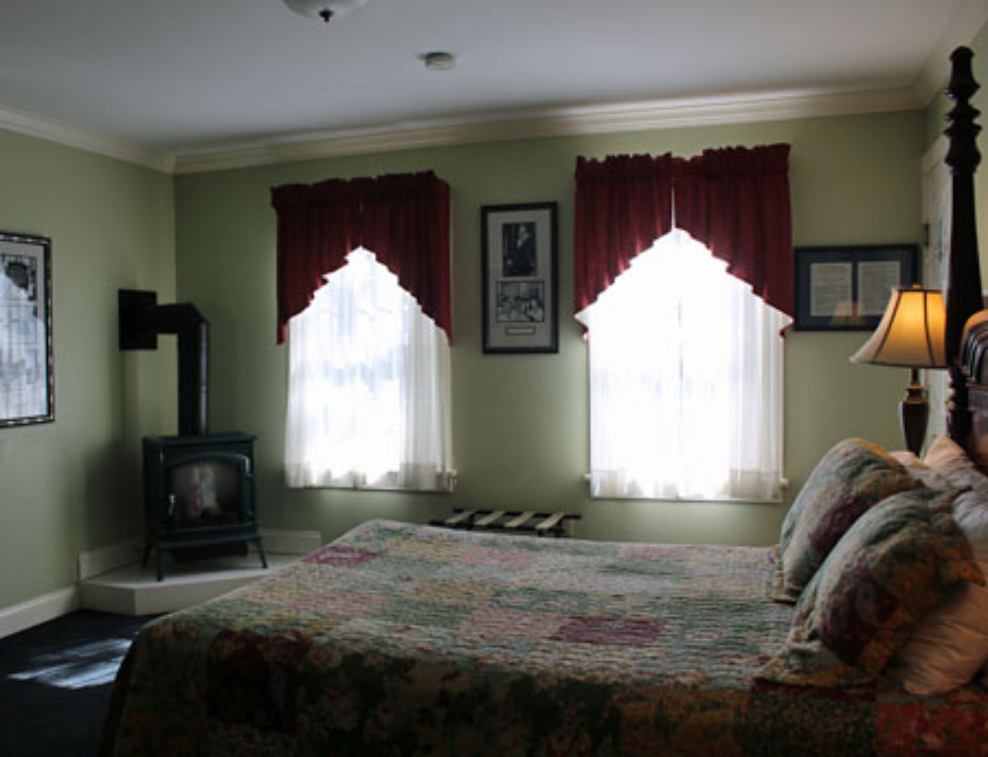 A bedroom with two windows, a bed with a floral bedspread, a dresser, and a lamp.