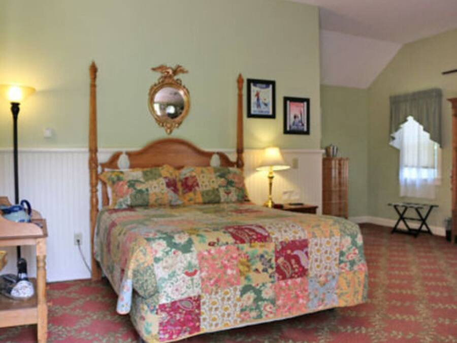 A bedroom with a wooden bed, floral bedding, a mirror above the bed, and a lamp on a bedside table.