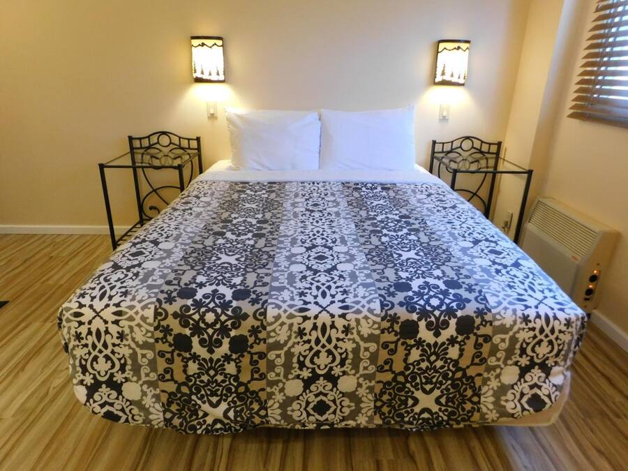 A bed with a patterned bedspread, two wall-mounted lamps, and a radiator.