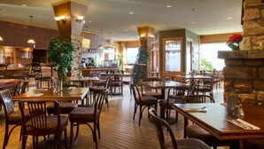 Un restaurant spacieux avec des tables et des chaises en bois, une cheminée en pierre et une grande plante.