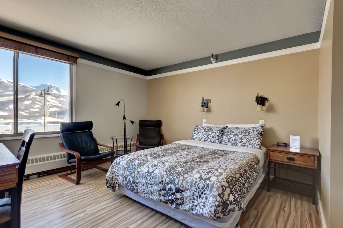 Une chambre d’hôtel avec un grand lit, un bureau, une chaise et une vue sur les montagnes par la fenêtre.