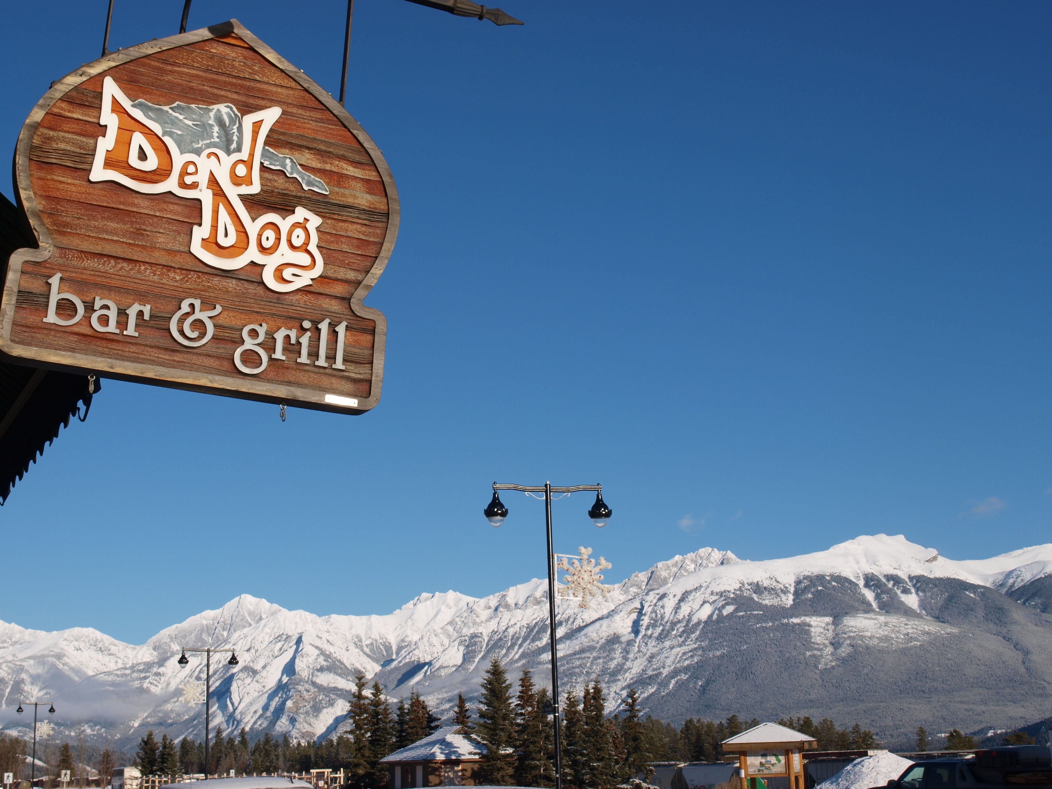 Une enseigne en bois indiquant « Dundog Bar & Grill », avec un paysage montagneux en arrière-plan.