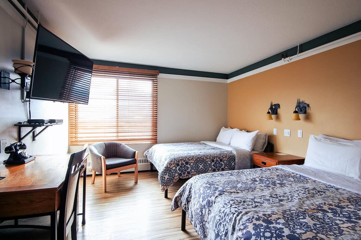 Une chambre d’hôtel avec deux lits, un bureau avec une chaise, une télévision et une fenêtre avec des stores.