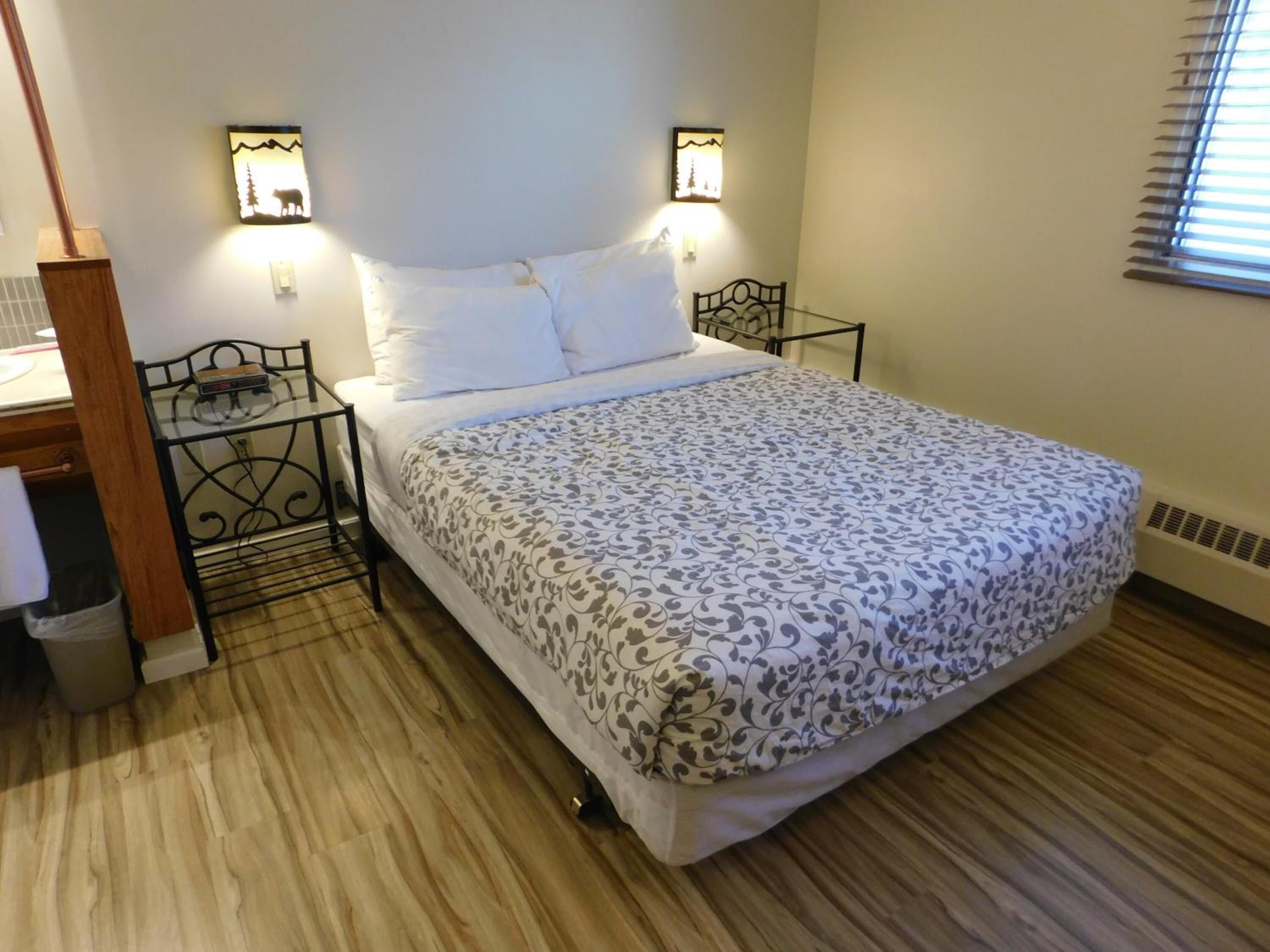 A neatly made bed with a patterned bedspread, two bedside tables with lamps, a wooden nightstand, and a radiator on the wall.