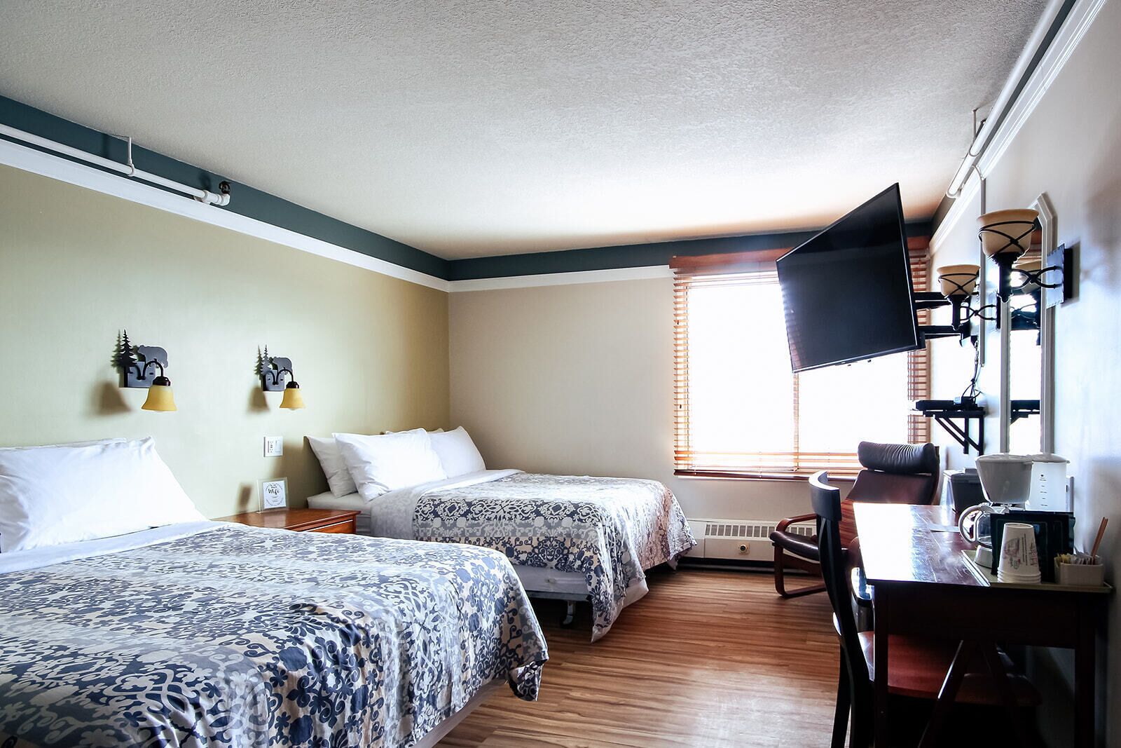 A hotel room with two beds, a desk with a coffee maker, and a TV mounted on the wall.