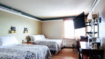 A hotel room with two beds, a desk with a coffee maker, and a TV mounted on the wall.