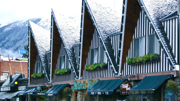 Une rangée de bâtiments aux toits à forte pente et aux éléments décoratifs en bois, avec des devantures de magasins portant des enseignes pour un restaurant et un bar.