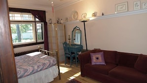 A bedroom with a bed, a desk, a chair, a red sofa, a ceiling fan, and a window with curtains. - Downtown Bed and Breakfast (Ottawa)