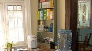 A kitchen with a water dispenser, a coffee maker, and a shelf with various items. - Downtown Bed and Breakfast (Ottawa)