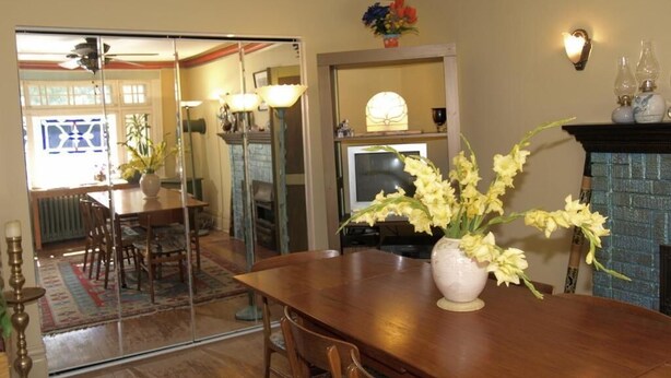A dining area with a wooden table, chairs, and a vase of flowers. There is a fireplace with a mantle and decorative items. - Downtown Bed and Breakfast (Ottawa)