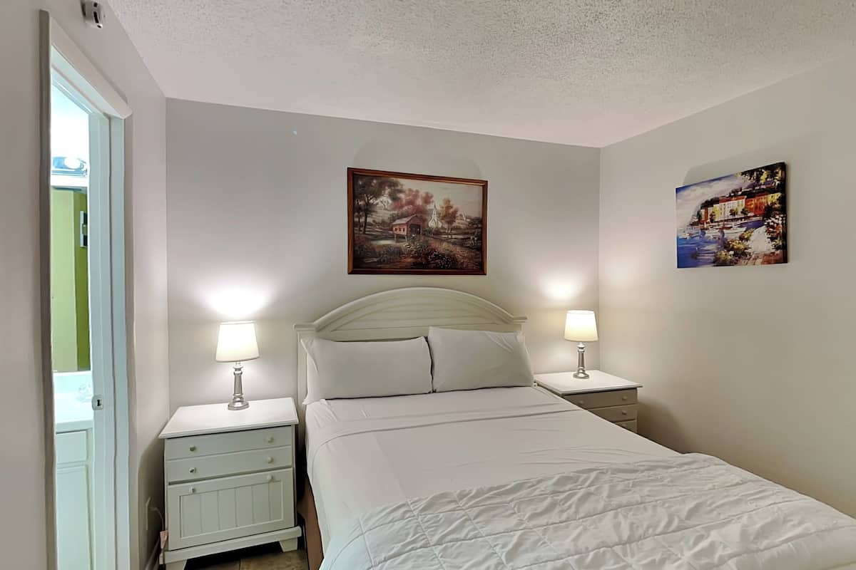 Une chambre à coucher comprenant un lit, deux tables de chevet avec des lampes, une commode, une coiffeuse et deux tableaux accrochés au mur.