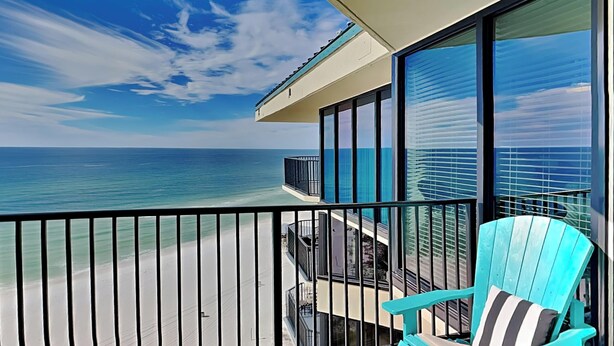 A balcony with a view of the ocean, a turquoise chair, and a modern building with large windows. - Sunbird Beach Resort by Resort Collection (Panama City Beach)