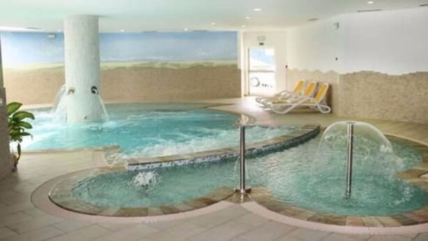Un área de spa con un jacuzzi, una piscina más pequeña y una zona de descanso con sillas.