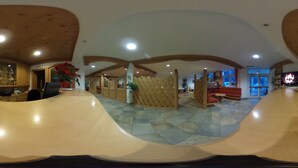 Un vestíbulo amplio con vigas de madera, una recepción, zona de estar y un ventanal grande.