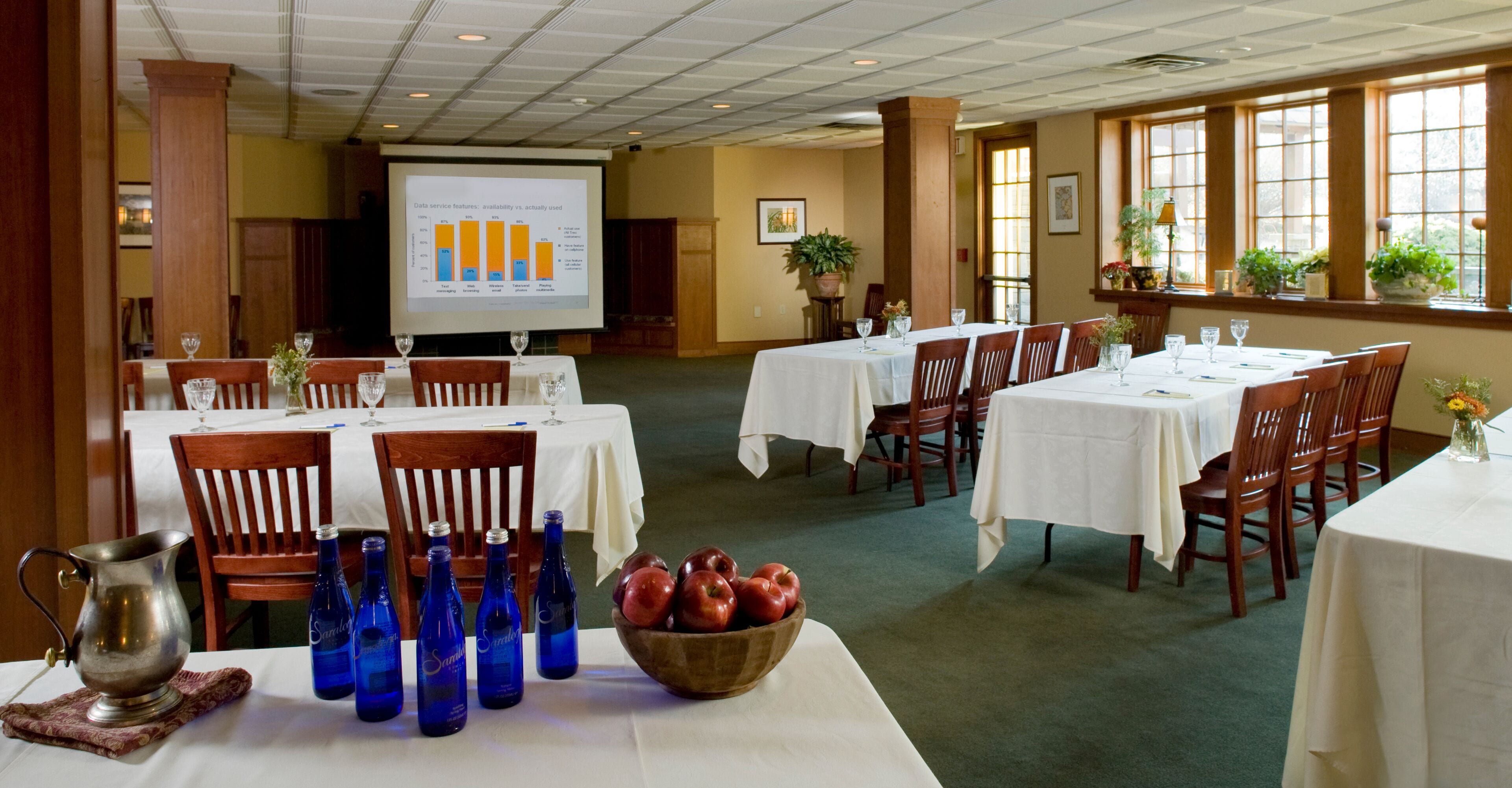 A conference room with tables set for a meeting, a projector screen displaying a graph, and a bowl of apples on one table.