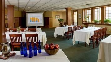 A conference room with tables set for a meeting, a projector screen displaying a graph, and a bowl of apples on one table.