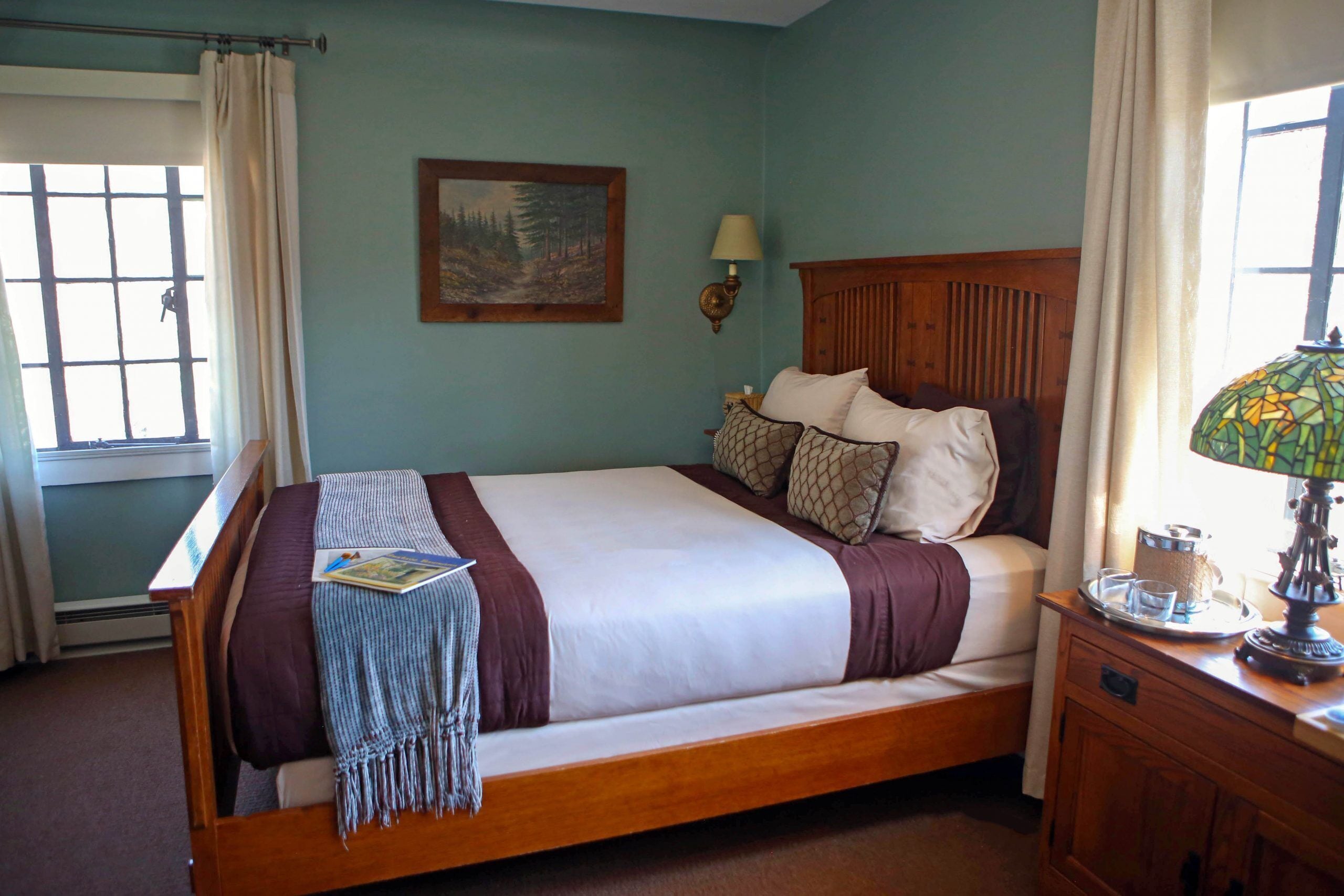 A neatly made bed with a wooden headboard, a bedside table with a lamp, and a window with curtains.