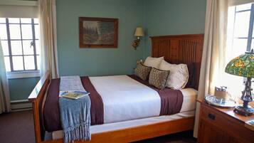 A neatly made bed with a wooden headboard, a bedside table with a lamp, and a window with curtains.