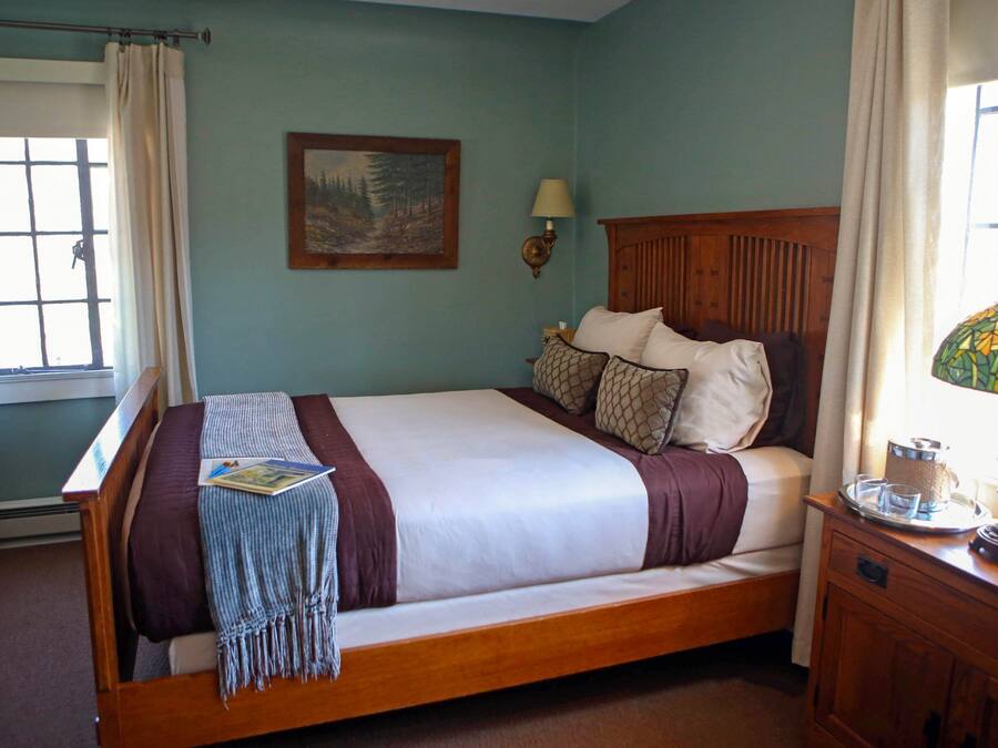 A neatly made bed with a wooden headboard, a bedside table with a lamp, and a window with curtains.