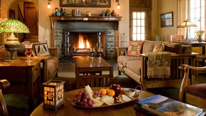 A cozy living room with a fireplace, wooden furniture, and a variety of snacks and drinks on a table.