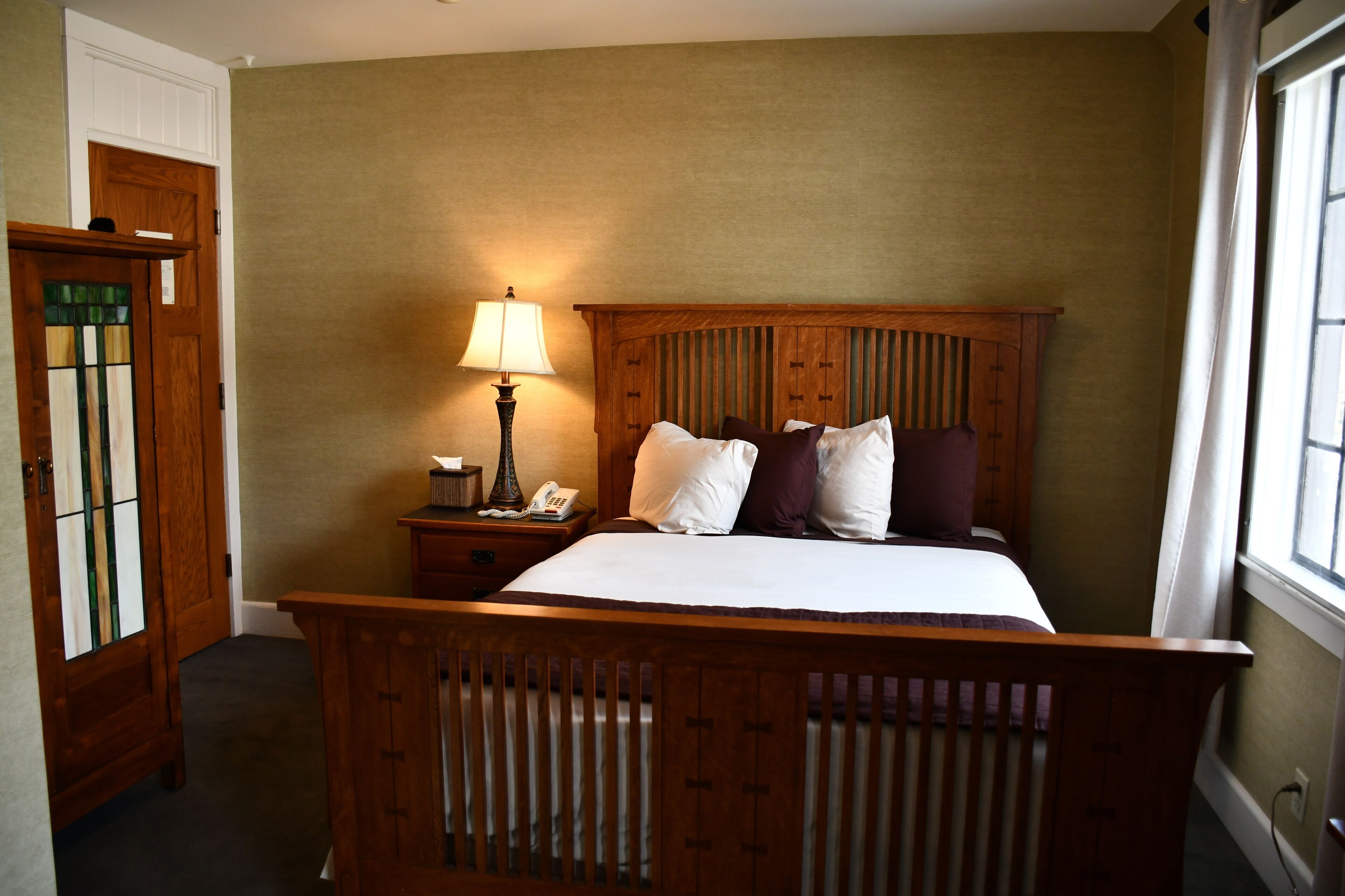 A bedroom with a wooden bed, a nightstand with a lamp, and a door with stained glass.