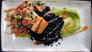 A plate with black rice, grilled chicken, a green salad, and a side of salsa.