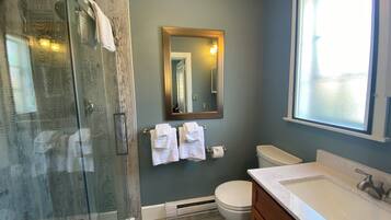 A bathroom with a glass-enclosed shower, a toilet, a sink with a marble countertop, and a mirror with a gold frame.