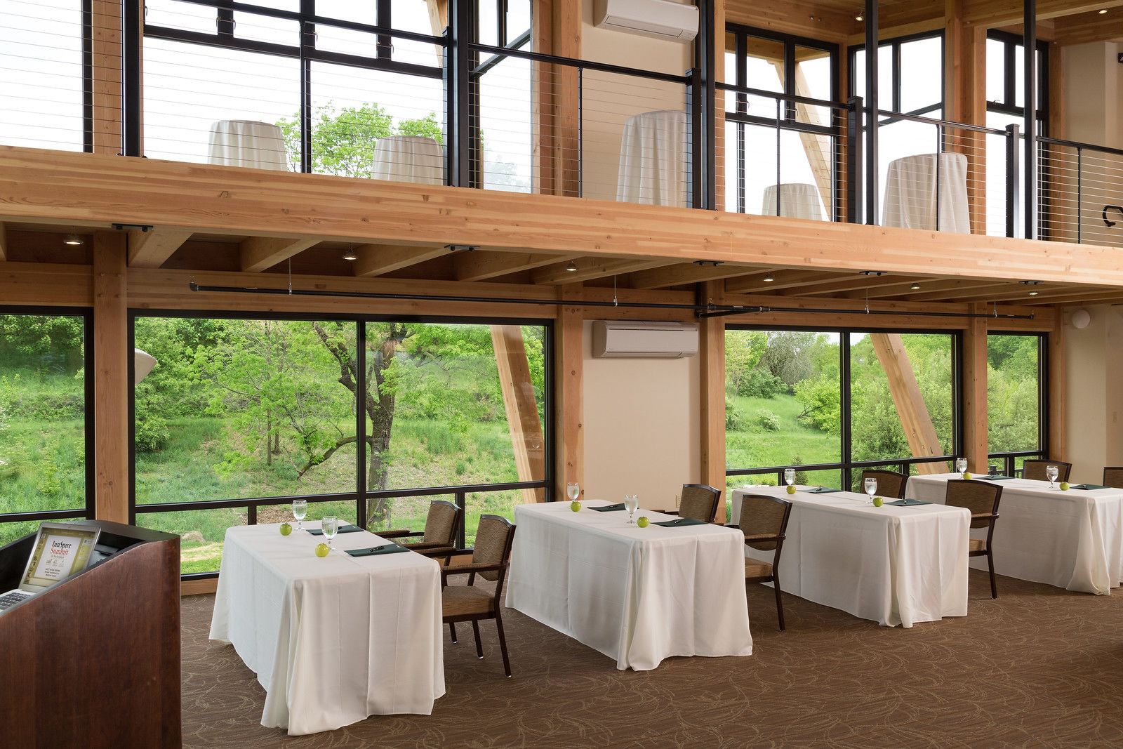 Ein Restaurant mit mehreren gedeckten Tischen, großen Fenstern mit Blick auf Grünflächen und einer Holzinnenausstattung.