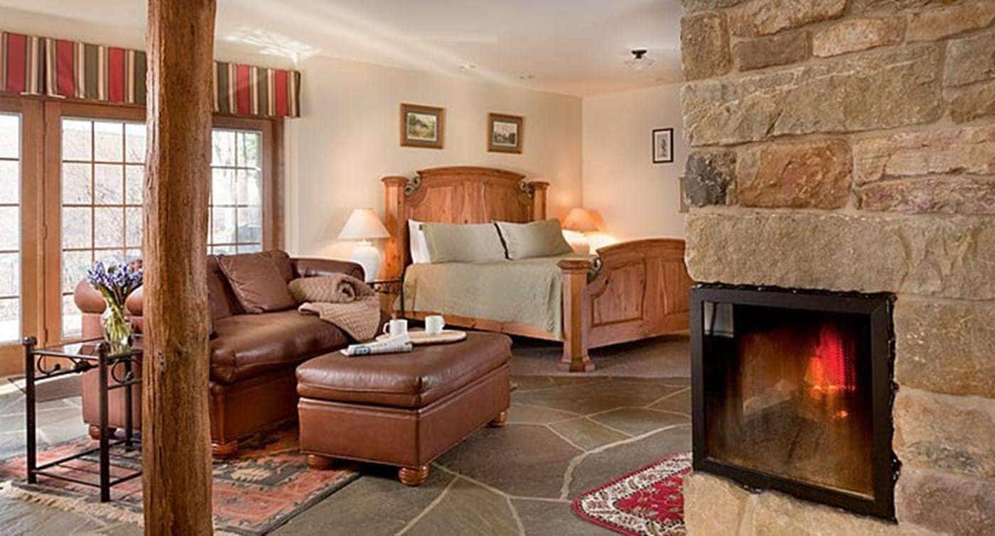 Una habitación acogedora con chimenea de piedra, una cama grande con cabecera de madera, un sofá de cuero y una pequeña mesa con un jarrón de flores.