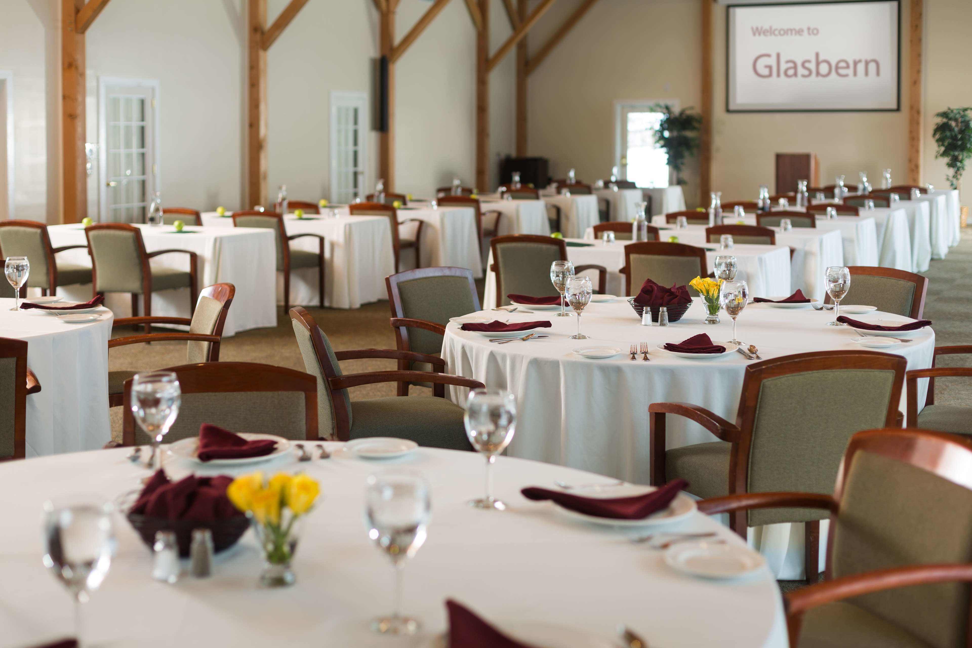 A banquet hall with round tables set for dining, featuring white tablecloths and neatly arranged place settings.