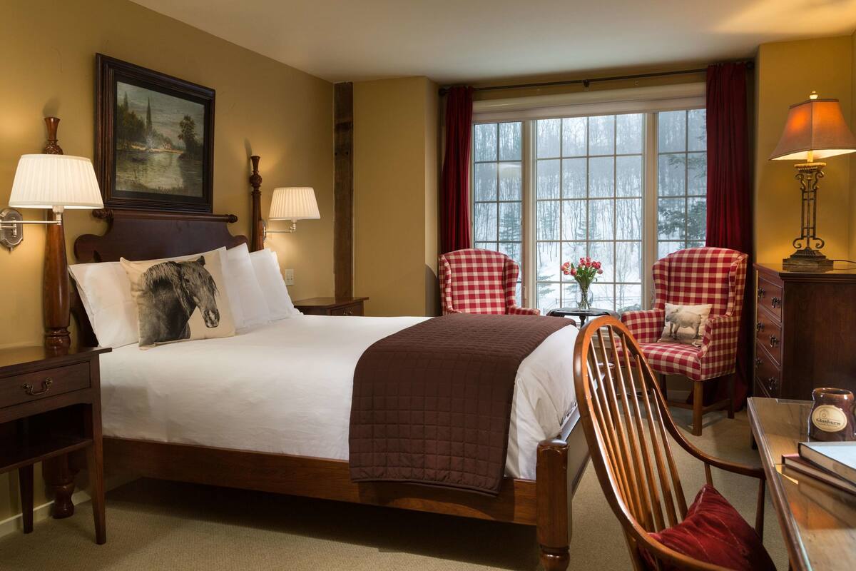 A neatly arranged bedroom with a large bed, a chair, a table, and a window with curtains.
