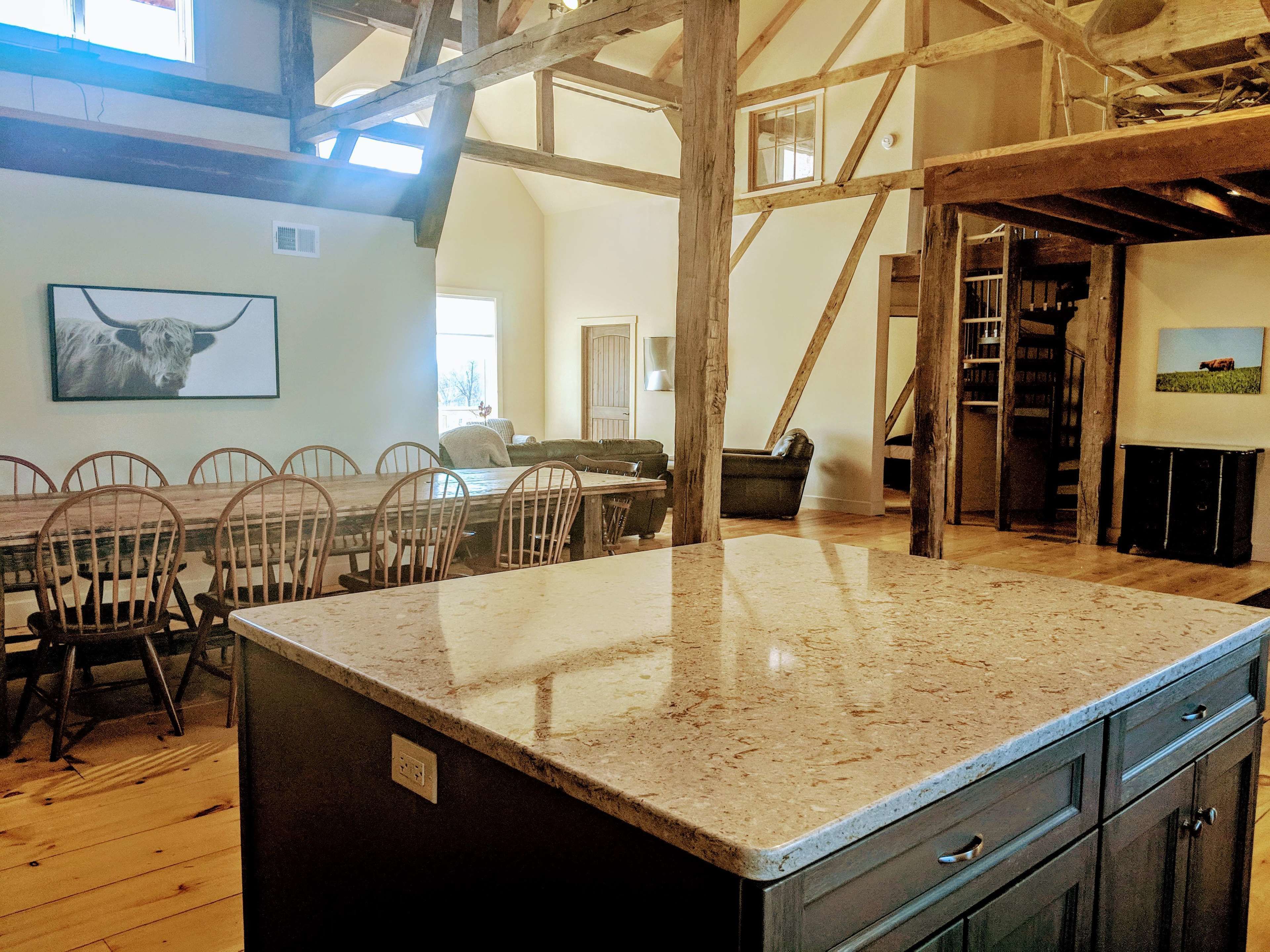A spacious kitchen with a large island, wooden chairs around a dining table, and a high ceiling with exposed beams.