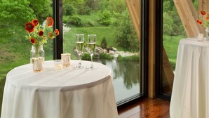 A round table with a white tablecloth, a vase with red flowers, two champagne flutes, and a candle.