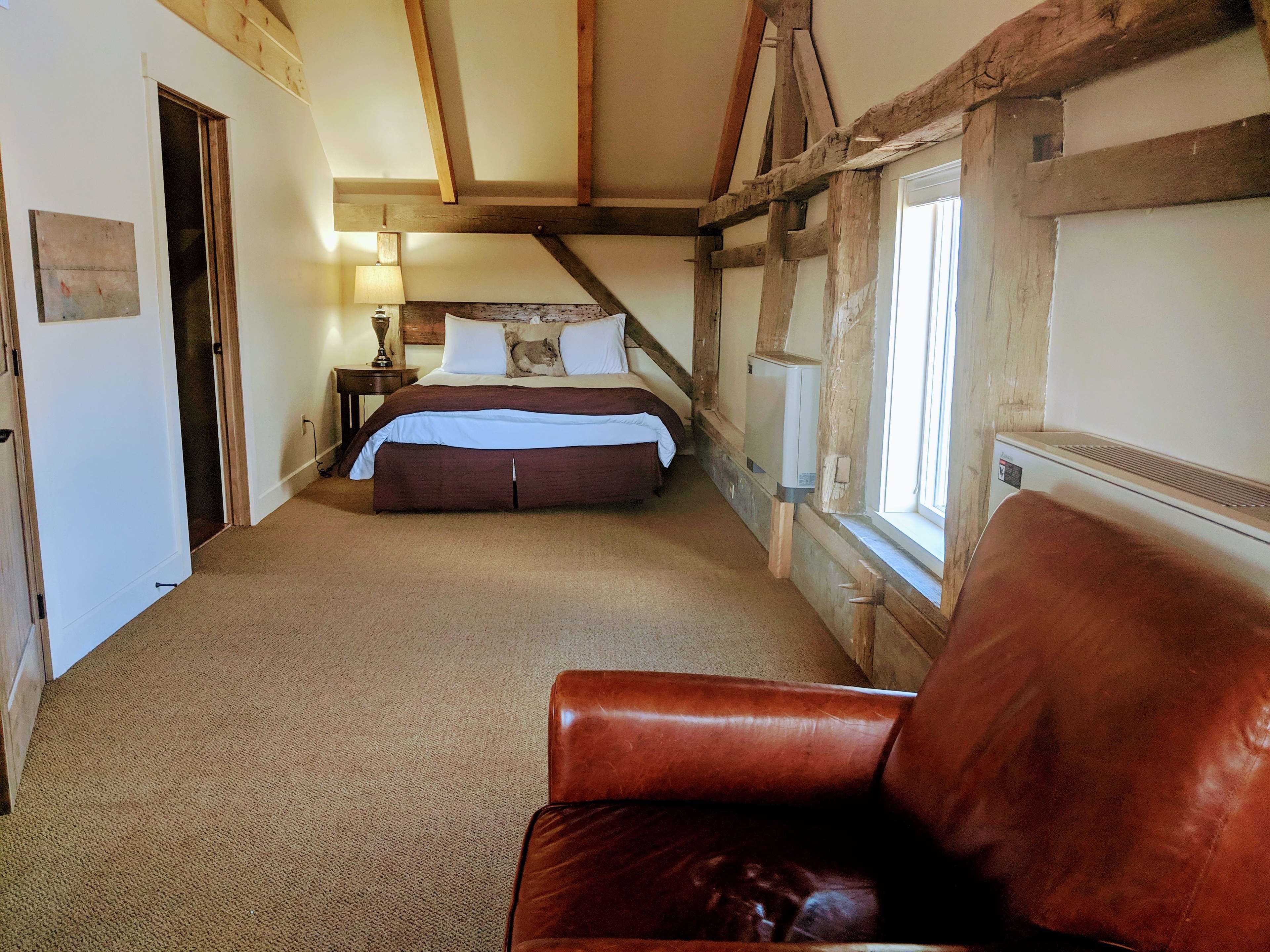A bedroom with a large bed, a wooden ceiling, a window, and a leather chair.