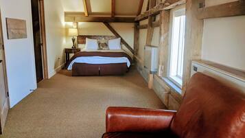A bedroom with a large bed, a wooden ceiling, a window, and a leather chair.