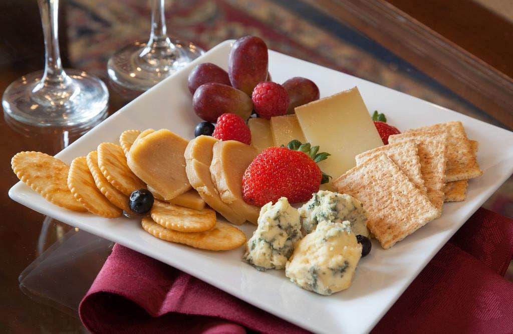 Een bord met kaas, crackers, aardbeien, druiven en een blauwe kaasdip op een wit bord.
