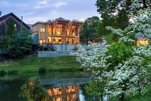 A modern house with a stone foundation, large windows, and a wooden deck overlooking a pond. - Glasbern - A Historic Hotel Of America (Fogelsville)