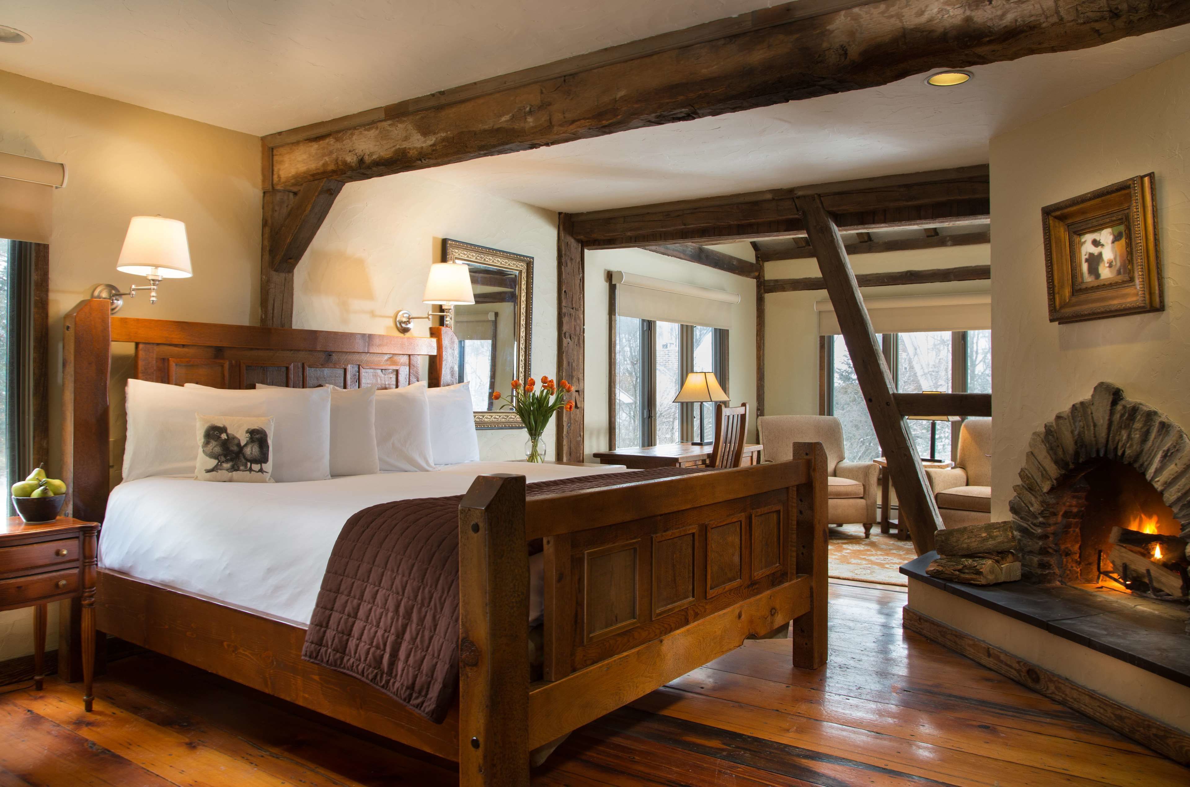 A bedroom with a large bed, wooden beams, a stone fireplace, and a view of the outdoors.