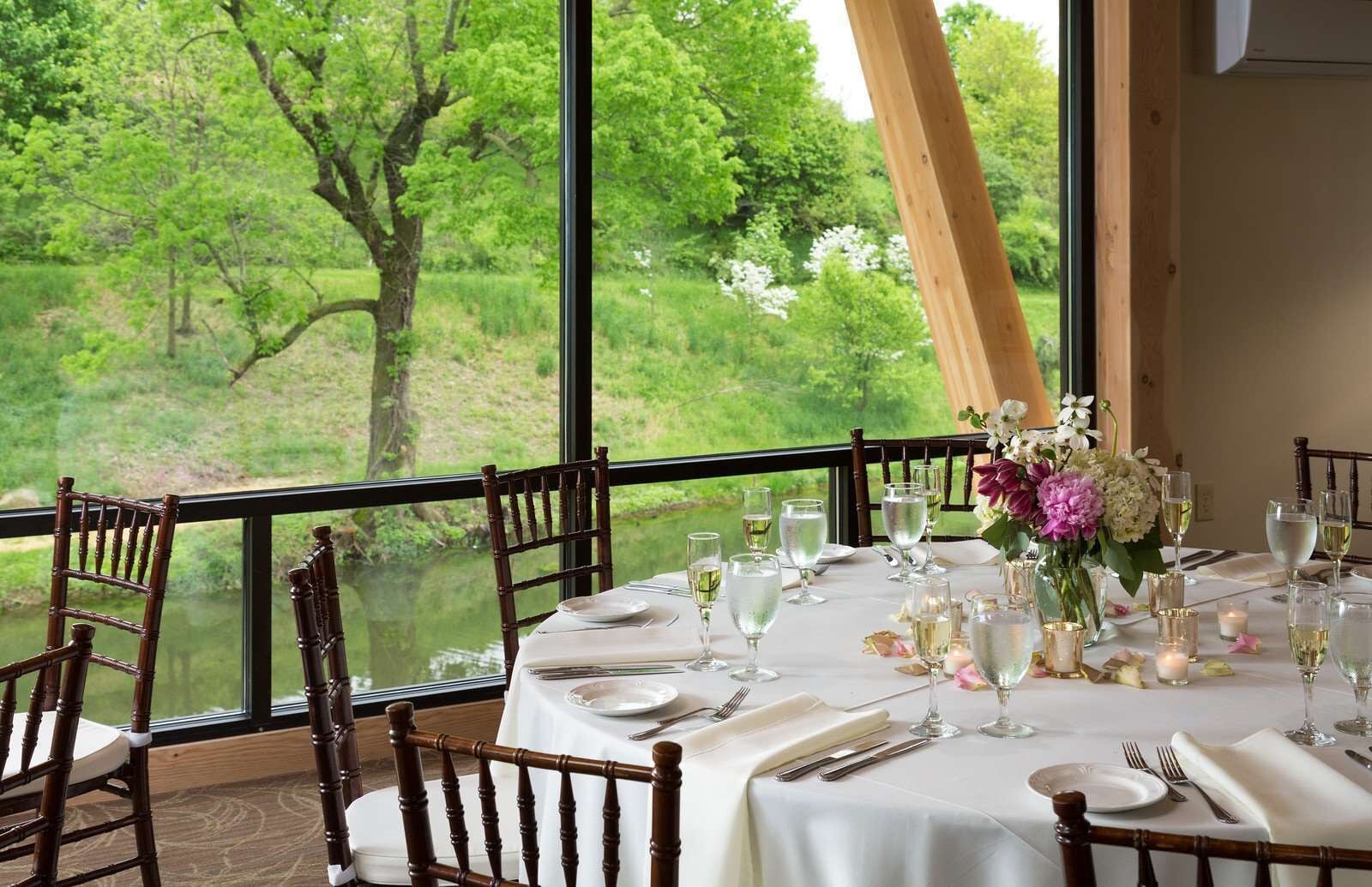A dining table set for six with a view of a lush green landscape through large windows.