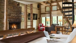 A cozy room with a stone fireplace, a wooden bench, a desk with a chair, and a spiral staircase.