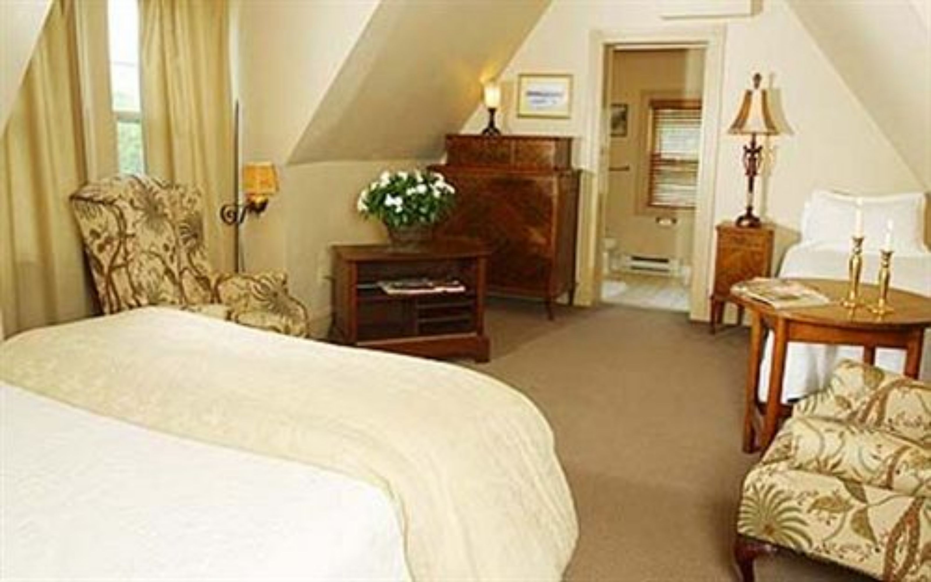 A hotel room with a large bed, a desk, a chair, a small table, and a lamp.