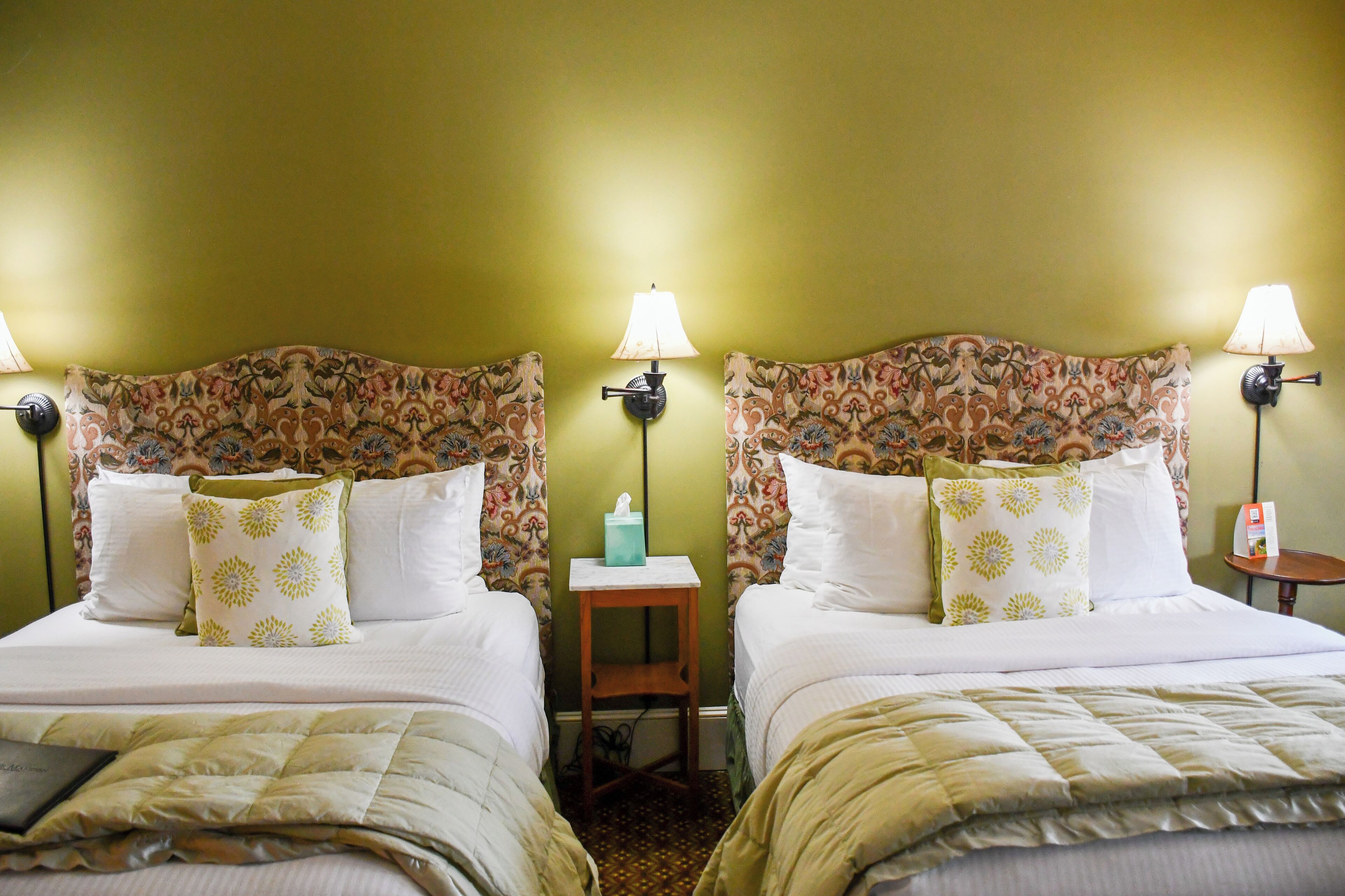 A hotel room with two beds, each with a floral headboard, bedside lamps, and matching pillows.