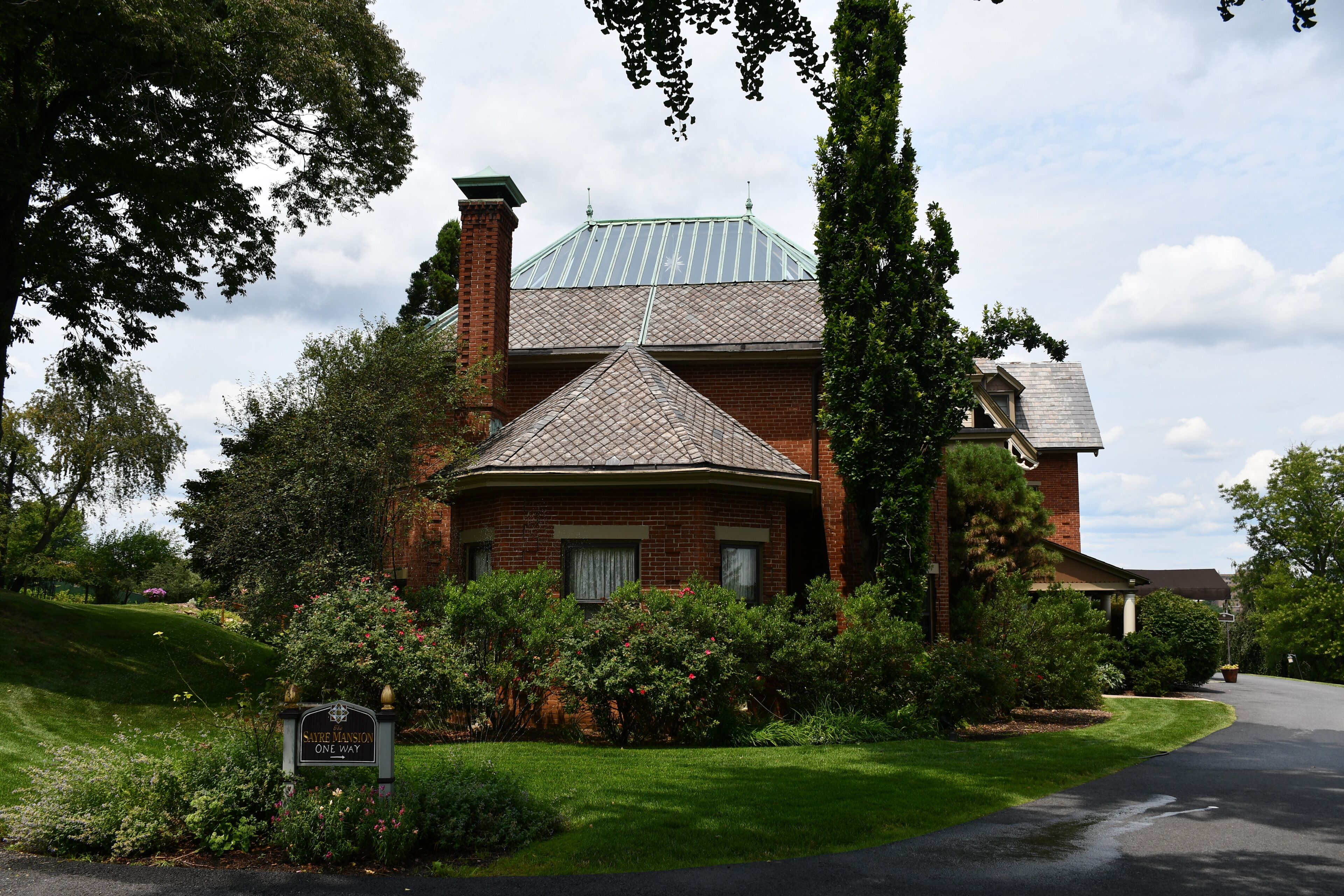 A brick house with a green roof, surrounded by lush greenery and a well-maintained lawn.